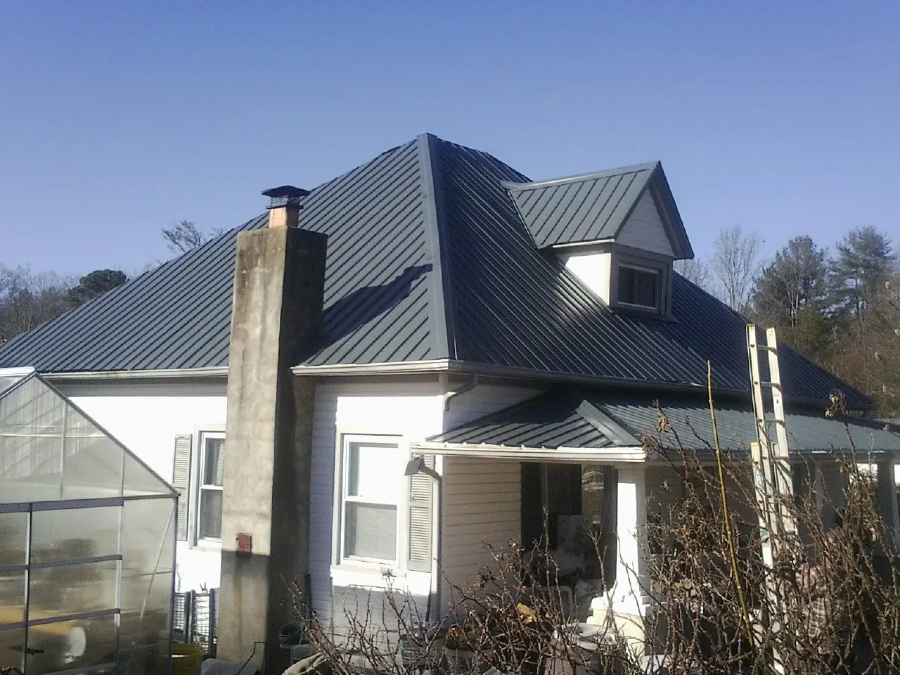 Dark blue standing seam metal roof on a white farmhouse with dormer — Slate & Tile Roof Repair by Roofing Brothers in Essig