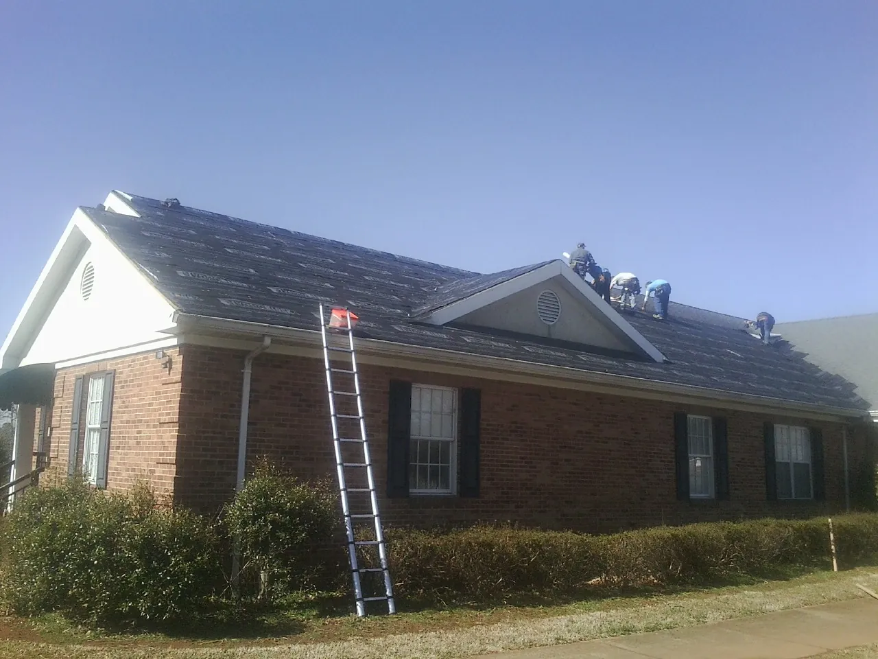 Crew tearing shingles off a brick ranch roof with a ladder set — Emergency Roof Repair work by our crew in Essig