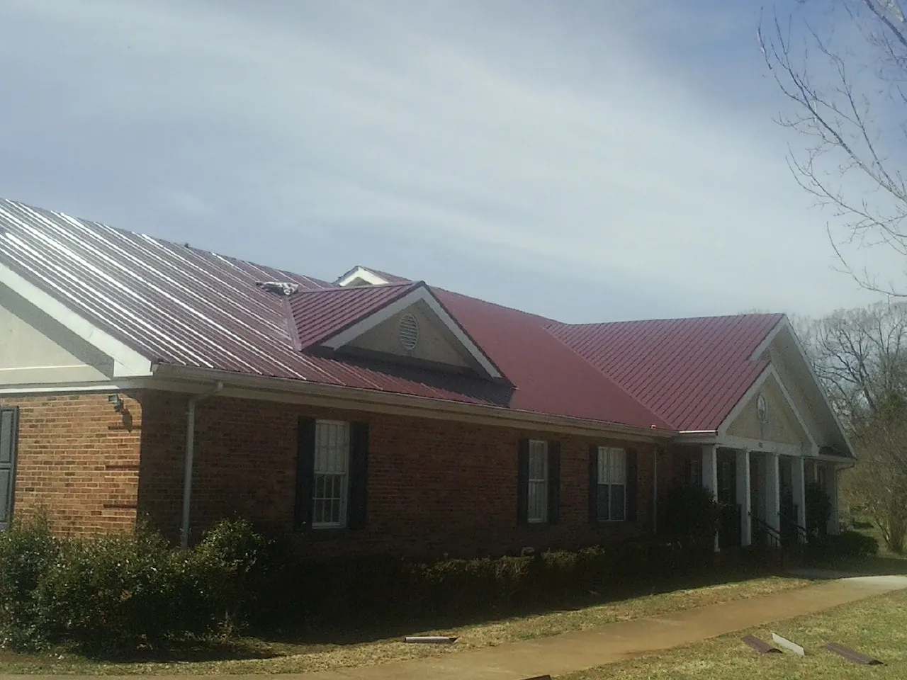 Red metal roof with gabled entries on a long brick building, from a Hail Damage Roof Repair job in Essig