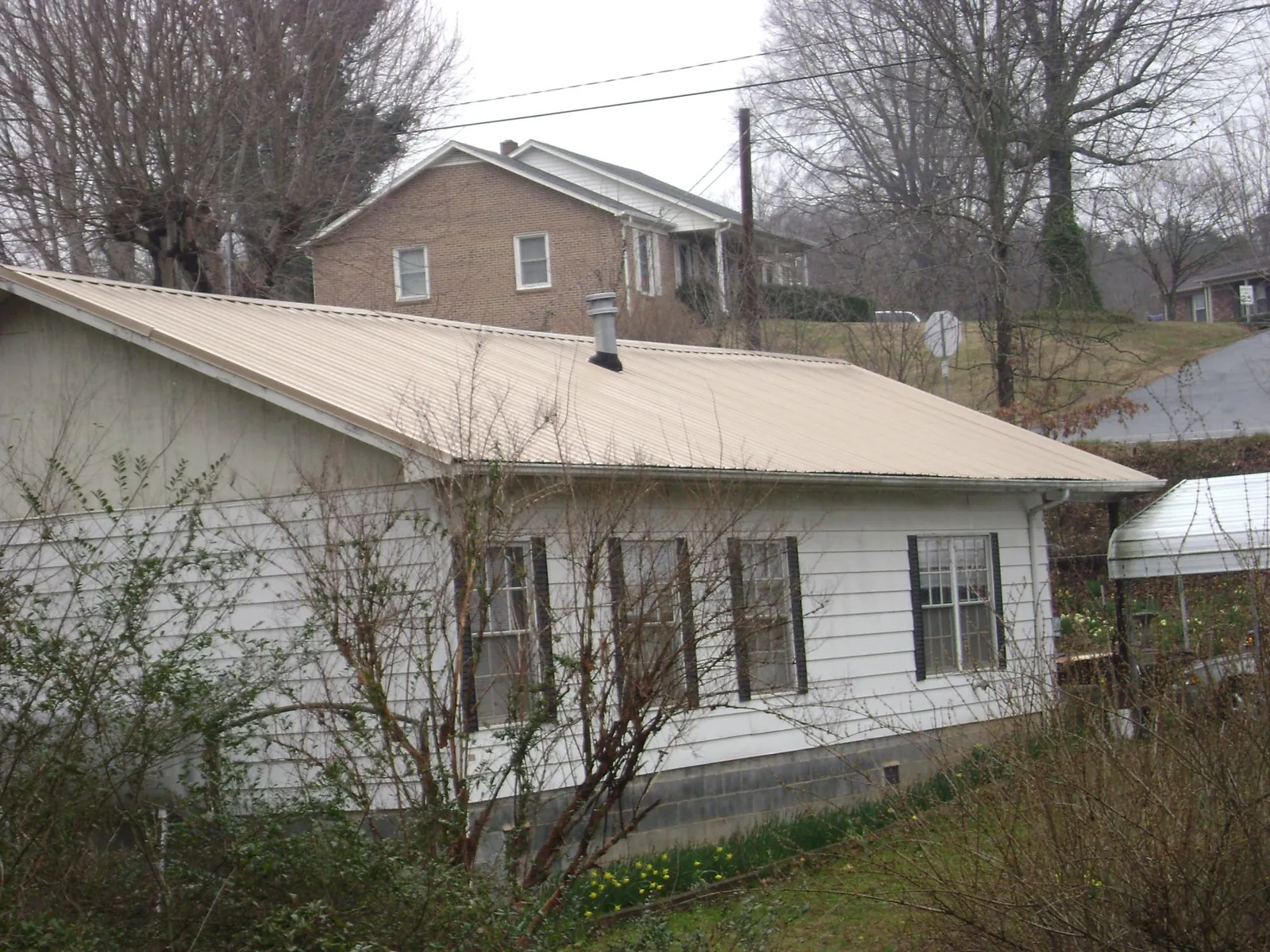 Tan metal roof on a white sided house set into a hillside — Commercial Roofing by Roofing Brothers in Essig